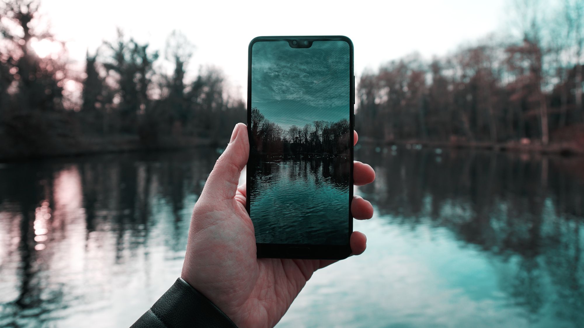 Рука держит смартфон на фоне реки